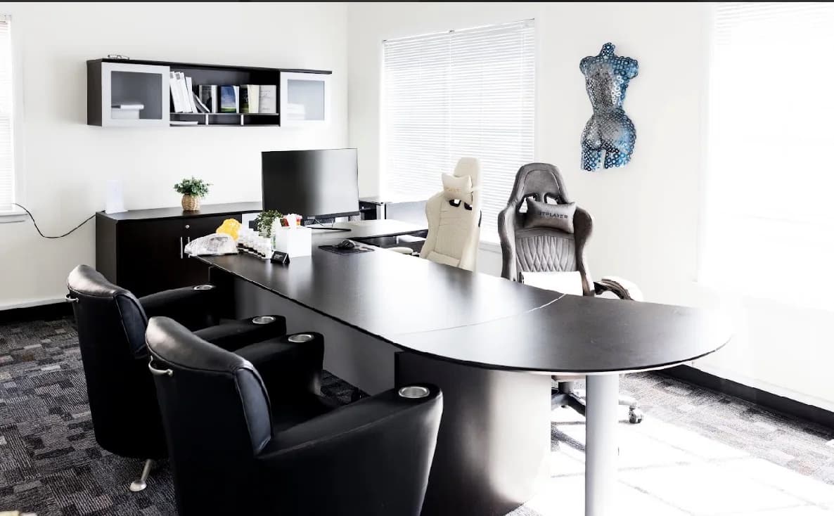 A bright office with a curved black desk and black armchairs beside large windows.