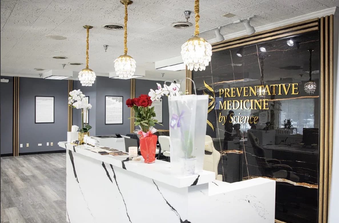 The front reception desk: a white marble counter with black veining, brass pendant lights, and the practice name in gold on a black glass wall.